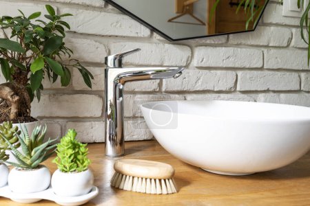 Téléchargez les photos : Évier en céramique sur comptoir en bois dans une salle de bain avec mur de briques blanches, plantes et miroir à l'intérieur industriel de la salle de bain. - en image libre de droit