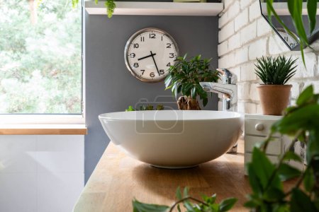 Téléchargez les photos : Salle de bain avec lavabo élégant et robinet moderne sur un comptoir en bois avec des plantes vertes. Intérieur lumineux avec mur de briques et fenêtre. Spa à la maison. - en image libre de droit