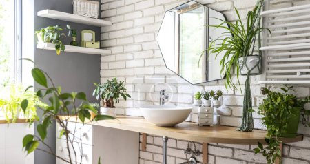 Téléchargez les photos : Intérieur de la salle de bain avec miroir sur un mur de briques blanches, mobilier élégant, lavabo à la mode et plantes vertes. Plante domestique et sp à la maison. Panoramique. - en image libre de droit