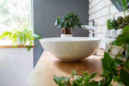 Téléchargez les photos : Spa moderne avec fenêtre et plantes vertes et plantes en pot et lavabo en céramique. Intérieur de la salle de bain avec mur de briques dans un style industriel. - en image libre de droit
