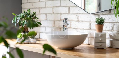Téléchargez les photos : Salle de bain intérieure avec mur de briques blanches, comptoir en bois avec lavabo élégant, miroir moderne et plantes vertes. Spa de bain dans un style industriel dans un appartement loft. - en image libre de droit