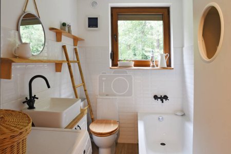 Photo for Bathroom with white tiles, window, stylish basin, round mirror, plants and wooden shelf in rustic style. Interior of vintage cottage. - Royalty Free Image
