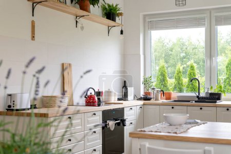Foto de Moderno interior de cocina blanca con ventana en estilo rural. Muebles de madera, encimera, estufa y plantas en cocina de diseño. Interior con estilo. - Imagen libre de derechos