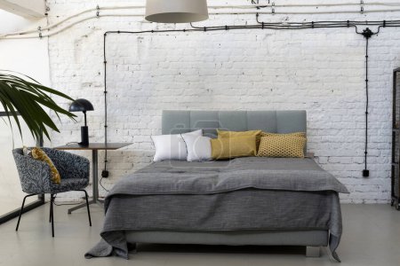 Photo for Industrial interior of bedroom in scandinavian style with grey bed, pillows and white brick wall with copy space. Indoors architecture design. - Royalty Free Image