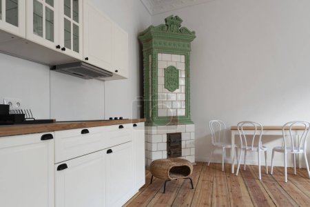 New modern apartment in industrial loft with white wall, wooden floor, ceramic tiled stove, kitchen and table with chairs. Dining room and living room in spacious indoors in townhouse.