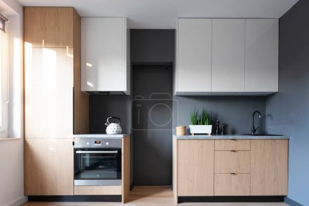Foto de Interior moderno de la cocina con muebles blancos y gabinete elegante de madera y pared gris. Acogedor piso en estilo minimalista. Nueva casa contemporánea - Imagen libre de derechos