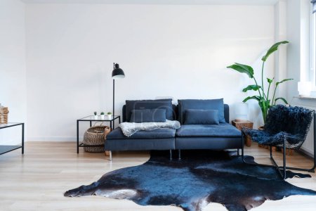 Moderno salón con cómodo sofá y sillón y pared blanca con espacio para copiar. Suelo de madera con cuero. Estilo miminalista en la habitación. Copiar espacio.