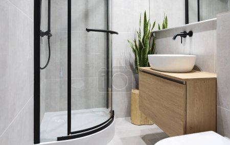 Téléchargez les photos : Salle de bain moderne avec carrelage gris, meubles en bois, douche, lavabo élégant et miroir. Intérieur industriel à la maison. - en image libre de droit