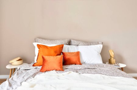 Foto de White and red pillows on a comfortable double bed in cozy interior of bedroom. Bedding and blanket in stylish design in modern room in hotel. New apartment. Copy space od the empty wall. - Imagen libre de derechos