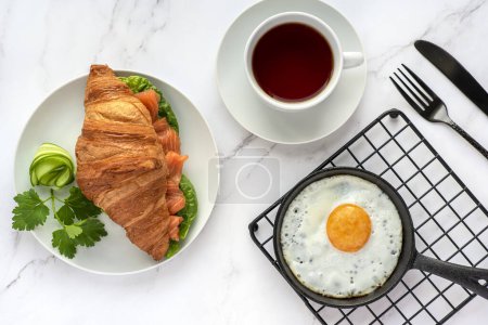 Téléchargez les photos : Photographie culinaire du petit déjeuner, croissant, oeuf frit, thé, sandwich au saumon - en image libre de droit