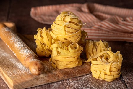 Photo for Food photography of  raw pasta, tagliatelle, fettuccine, macro, rolling pin, board - Royalty Free Image