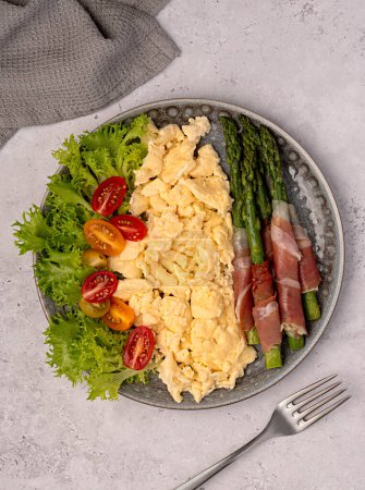 Photo for Food photography of breakfast, scrambled egg, fried asparagus, prosciutto, tomato, leaf, lettuce, brunch, fork, background, meal, food - Royalty Free Image