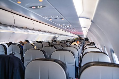 Téléchargez les photos : Intérieur des grands avions de passagers avec des personnes sur les sièges et hôtesse de l'air en uniforme marchant dans l'allée
. - en image libre de droit