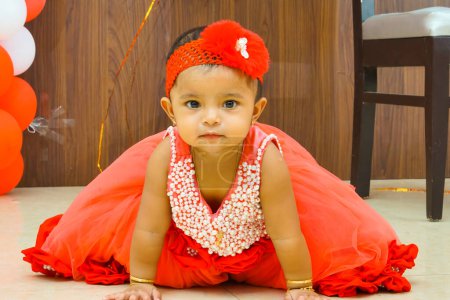 Photo for A cute Indian baby crawls on the floor in a red dress. The baby is smiling and looks happy - Royalty Free Image