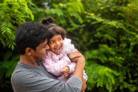 Téléchargez les photos : Une photo chaleureuse d'un père et d'une fille indiens souriant et jouant dans un parc par une journée ensoleillée. Le père tient celui de sa fille. - en image libre de droit