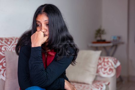 Una joven con el pelo largo está sentada en un sofá, triste y abatida
