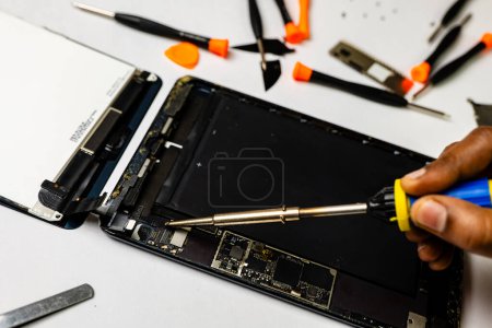Photo for Technician meticulously solders a tablet component using specialized tools in a well-lit workspace - Royalty Free Image