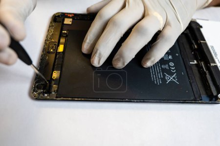 Téléchargez les photos : Un technicien concentré démonte méticuleusement une tablette en utilisant une variété d'outils spécialisés - en image libre de droit