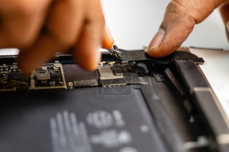Photo for Technician carefully removes the damaged ribbon from a tablet using specialized tools - Royalty Free Image