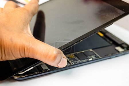 Téléchargez les photos : Un technicien qualifié sépare méticuleusement l'écran fissuré d'un appareil tablette à l'aide d'outils spécialisés - en image libre de droit