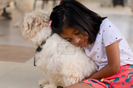 An adorable image of a young girl sitting on the floor, hugging her beloved dog tightly with her eyes closed