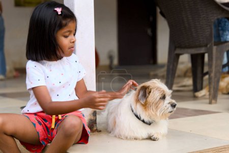 A close-up photo of a happy Asian girl enjoying playtime with her adorable pet dog at home