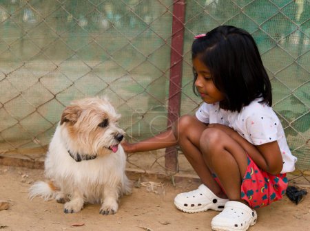 A heartwarming image of a young girl kneeling down to pet a friendly dog at an animal shelter.