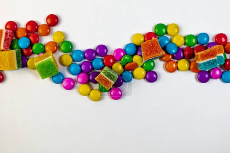 A burst of colorful candies in various shapes and sizes, scattered across a clean white background. Top view