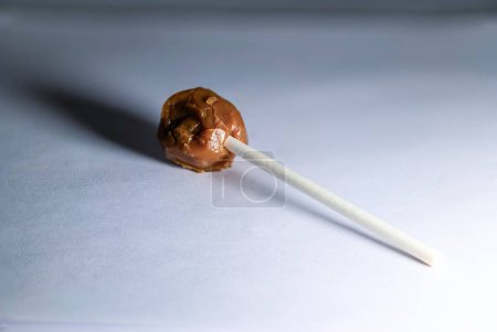 A mouthwatering chocolate lollipop with a smooth, glossy surface, captured in sharp focus on a white background