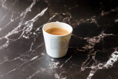 Ein wunderschön komponiertes Bild, das eine dampfende Tasse Kaffee zeigt, die auf einer polierten schwarzen Marmoroberfläche ruht