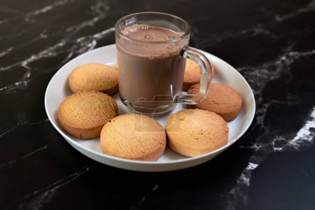 Photo for A luxurious scene featuring a steaming mug of hot chocolate beside a plate of delectable cookies on a chic black marble surface - Royalty Free Image