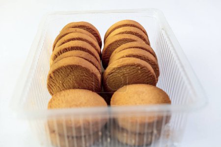 A close-up view of a variety of cookies in a clear plastic storage container, isolated on a white background.