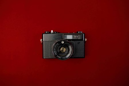 Une photo haute résolution montrant un appareil photo classique à film noir reposant sur une surface rouge vibrante