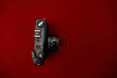 Ein hochauflösendes Foto, das eine klassische schwarze Vintage-Filmkamera zeigt, die flach auf einem lebhaften roten Hintergrund ruht