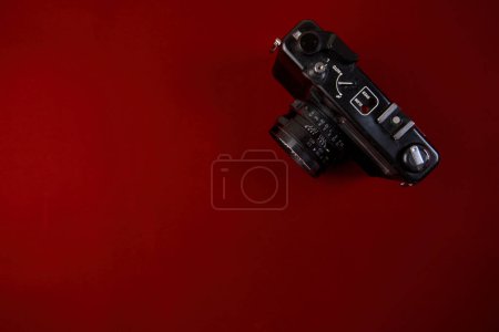 Una foto de alta resolución que muestra una clásica cámara de película negra apoyada sobre una superficie roja brillante