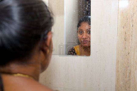 A woman gazes into a bathroom mirror, her reflection staring back