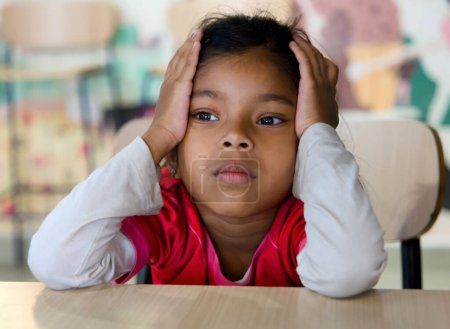 Une jeune fille de l'école primaire avec une expression inquiète s'assoit seule à son bureau