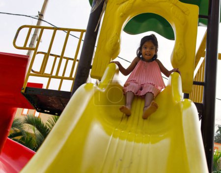 Ein unbeschwertes junges Mädchen lacht vor Freude, als sie auf einem sonnigen Spielplatz eine bunte Rutsche hinunterzoomt