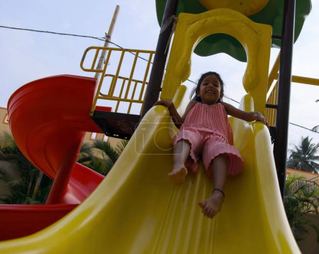 A young girl laughs with delight as she zooms down a colorful slide at a sunny playground