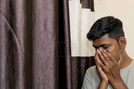 Ein nachdenkliches Porträt eines jungen indischen Mannes, dessen Hand sein Gesicht verdeckt, vielleicht Ausdruck von Traurigkeit