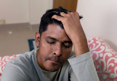 Ein junger Mann reibt sich beunruhigt die Stirn und hat Kopfschmerzen, wenn er drinnen sitzt.