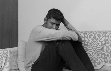 Schwarz-weiß Ein junger indischer Mann sitzt auf einem Sofa, nachdenklich und tief in Gedanken. Sein Gesichtsausdruck traurig