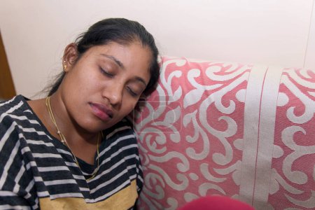 Photo for An image of a young Indian woman sleeping on a couch in her living room, seemingly tired - Royalty Free Image