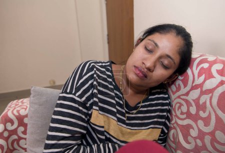 Photo for An image of a young Indian woman sleeping on a couch in her living room, seemingly stressed or upset - Royalty Free Image
