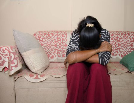 junge Frau sitzt allein auf einer Couch, den Kopf gesenkt in einem Blick der Enttäuschung oder Traurigkeit