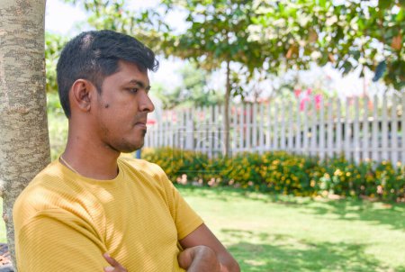 Un Indien assis sur un banc dans un jardin paisible, perdu dans la pensée par une journée ensoleillée.