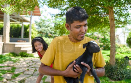 A delightful image of an Indian father and his daughter creating happy memories as they play with a charming young goat in their vibrant  backyard garden.