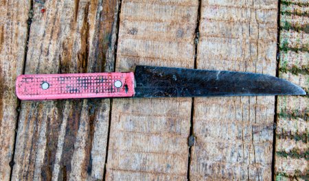 A close-up photo of a timeworn knife resting on a weathered wooden surface