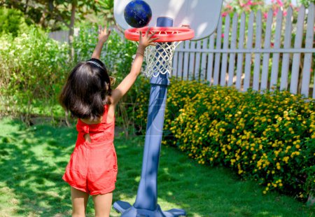 A  little girl with a determined expression dribbles a basketball on a sunny day in her backyard