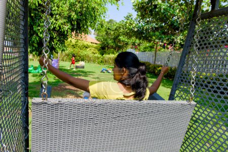 A carefree mother soars on a swing in her lush green backyard garden, bathed in the warm light of a beautiful day